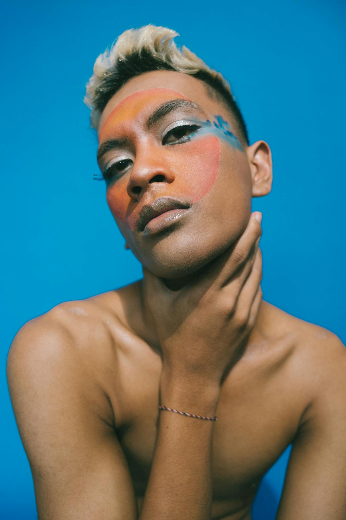 Colorful and creative portrait featuring bold makeup on a blue background, conveying artistic expression.