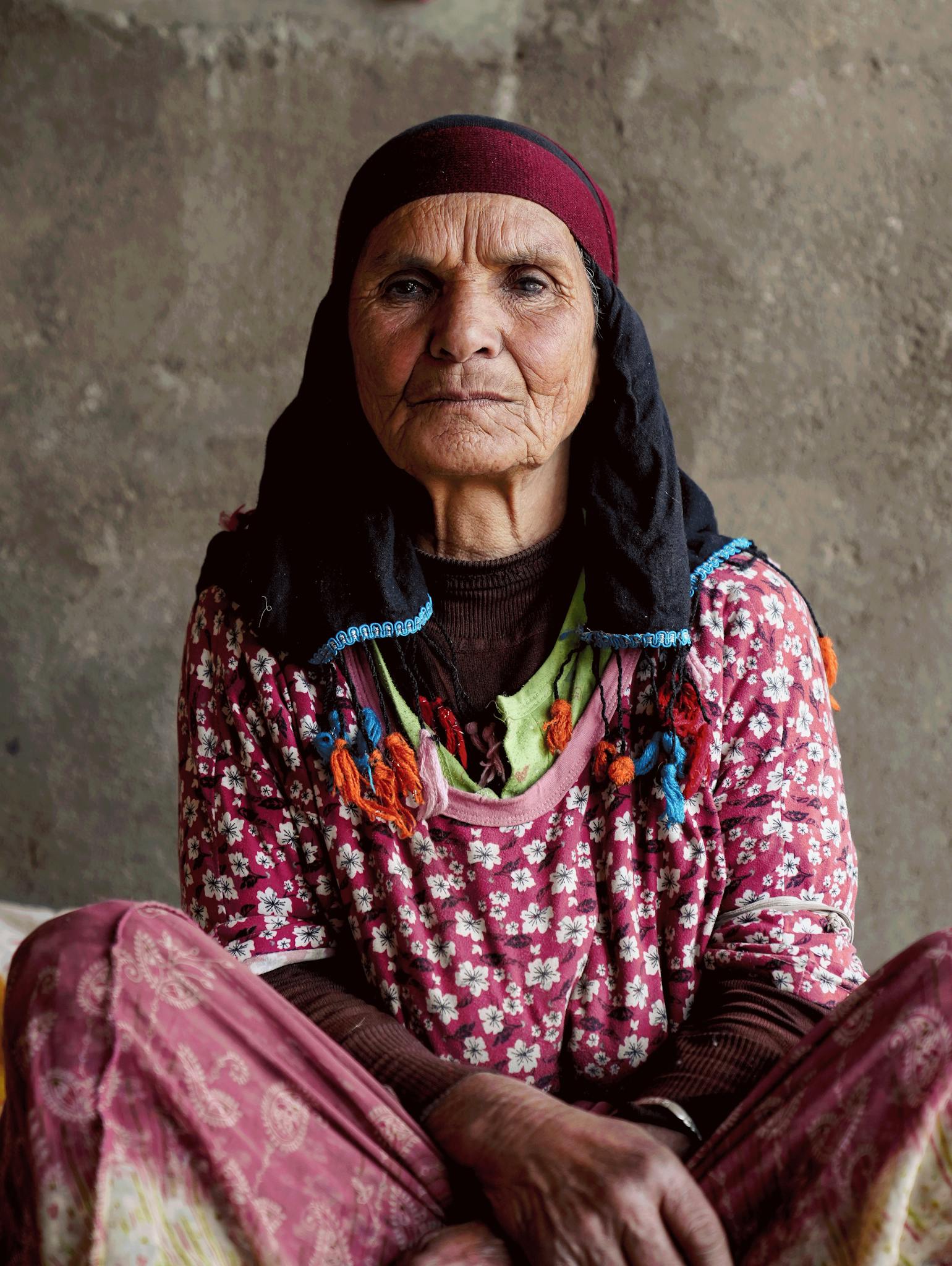 Elderly woman in traditional floral dress and headscarf, showcasing cultural heritage.